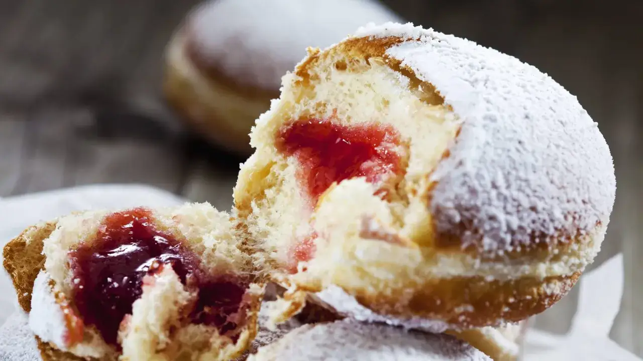 Ein aufgeschnittener Berliner Pfannkuchen mit Marmeladenfüllung, bestäubt mit Puderzucker.