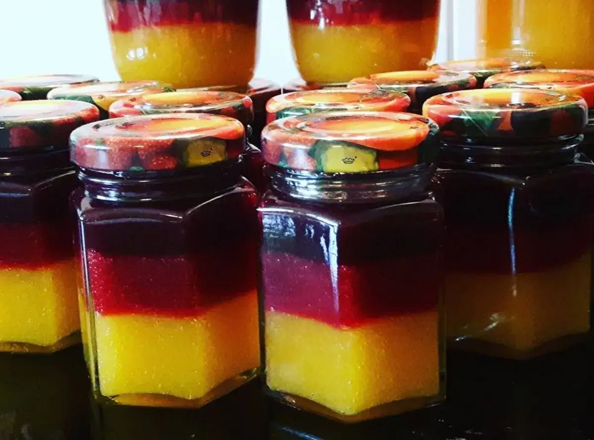 Mehrere Gläser mit geschichteter Marmelade, die an ein Kirschmarmelade Rezept erinnern. Unten gelb, dann rot, dann dunkelrot.
