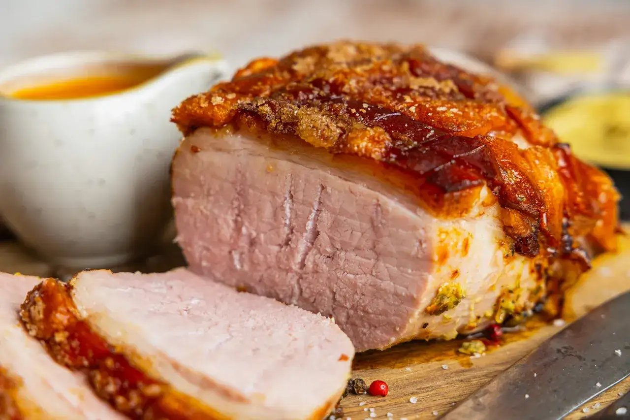 Saftiger Braten mit knuspriger Kruste, perfekt für die Zubereitung von Prager Schinken im Backofen. Dazu eine Schüssel mit Sauce.