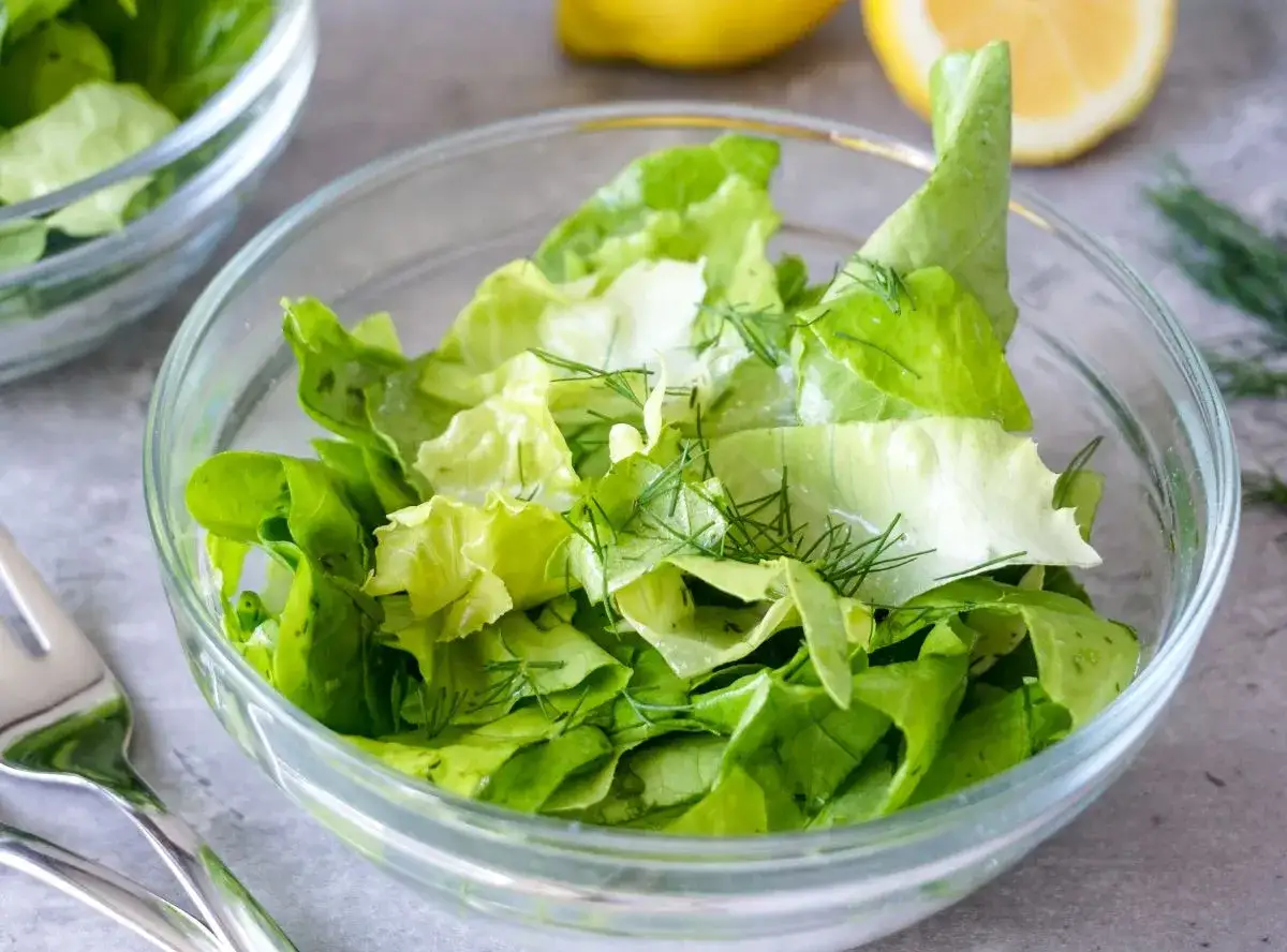 Frischer Kopfsalat mit Dill in einer Glassch&uuml;ssel, bereit f&uuml;r ein leichtes Kopfsalat Rezept. Zitronen im Hintergrund.