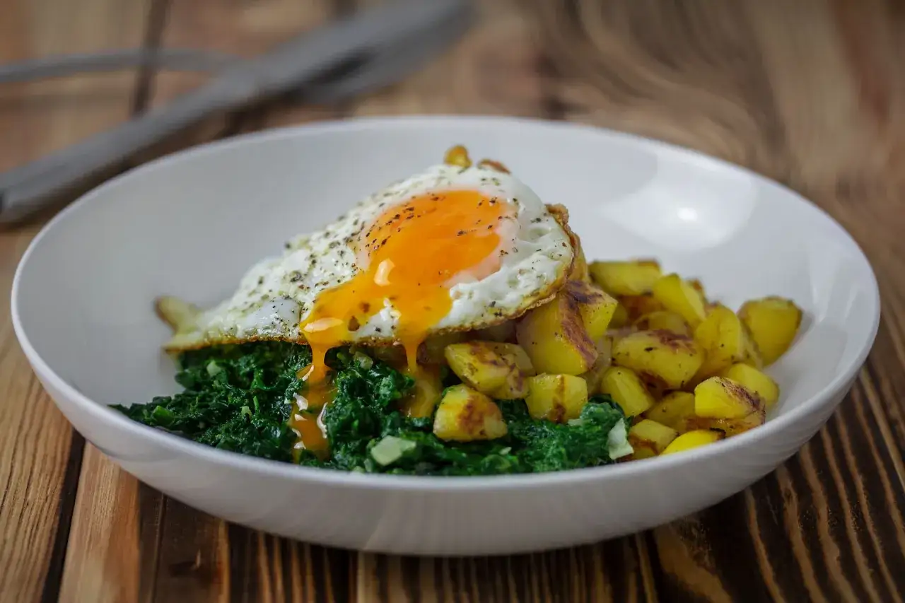 Ein leckeres Spinat-Rezept: Gebratener Spinat mit Kartoffeln und einem Spiegelei, dessen flüssiges Eigelb über das Essen läuft.