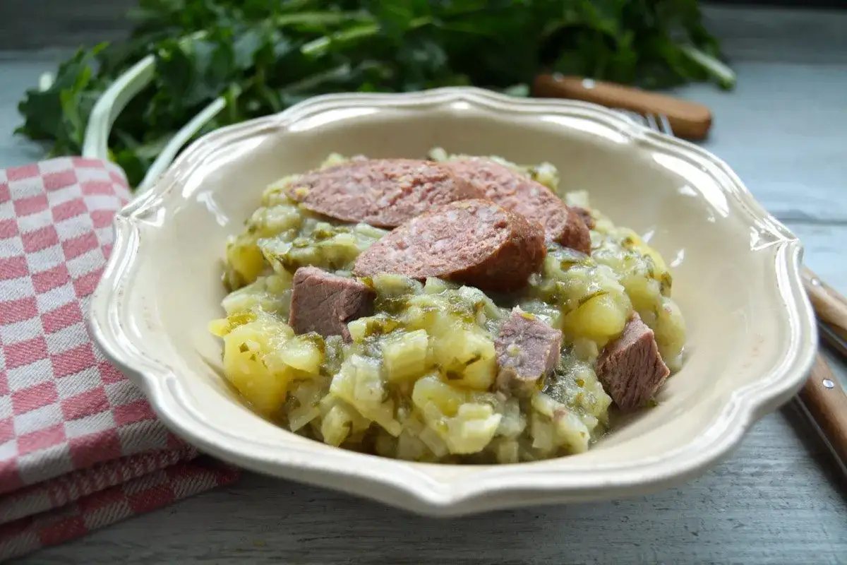 Herzhaftes Stielmus-Rezept von Oma: Kartoffeln, Fleisch und Wurst in einer Schüssel, serviert mit einem karierten Tuch.
