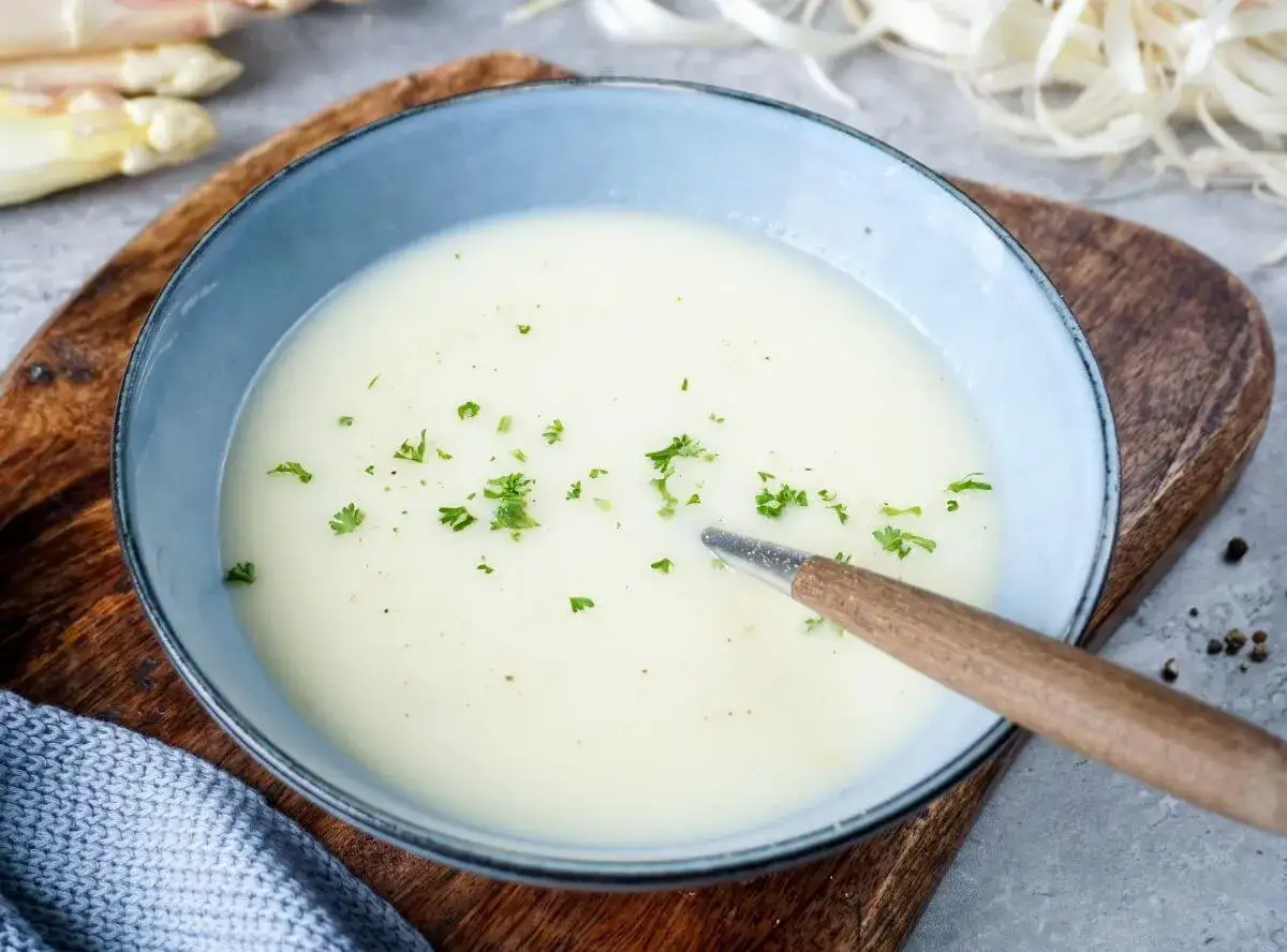 Cremige Spargelsuppe aus Schalen, garniert mit Petersilie, in einer blauen Schüssel auf einem Holzbrett.