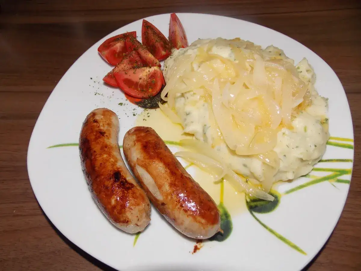 Zwei Bratwürste mit cremigem Kartoffelbrei, garniert mit Zwiebeln und Tomaten. Ein klassisches Kartoffelbrei Rezept von Oma.