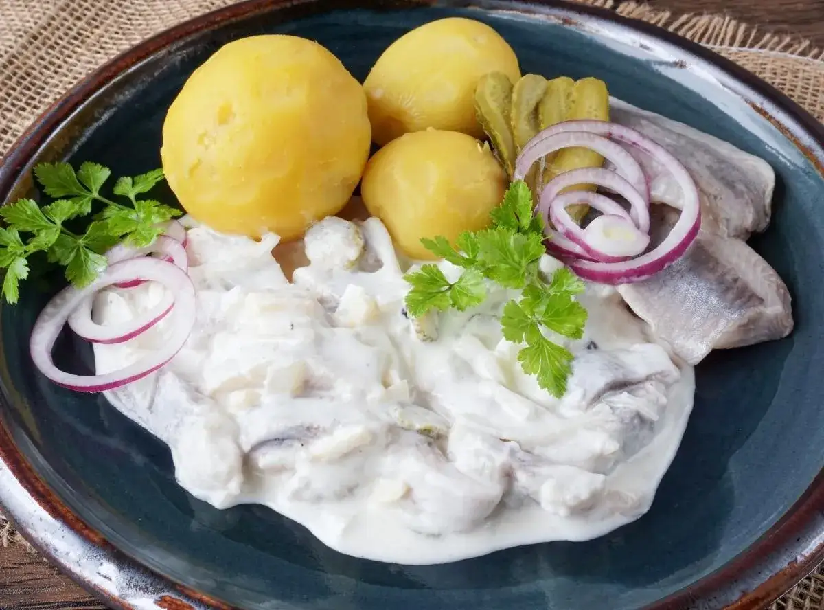 Marinierter Hering in cremiger Sauce mit Salzkartoffeln, Gurken und Zwiebelringen.