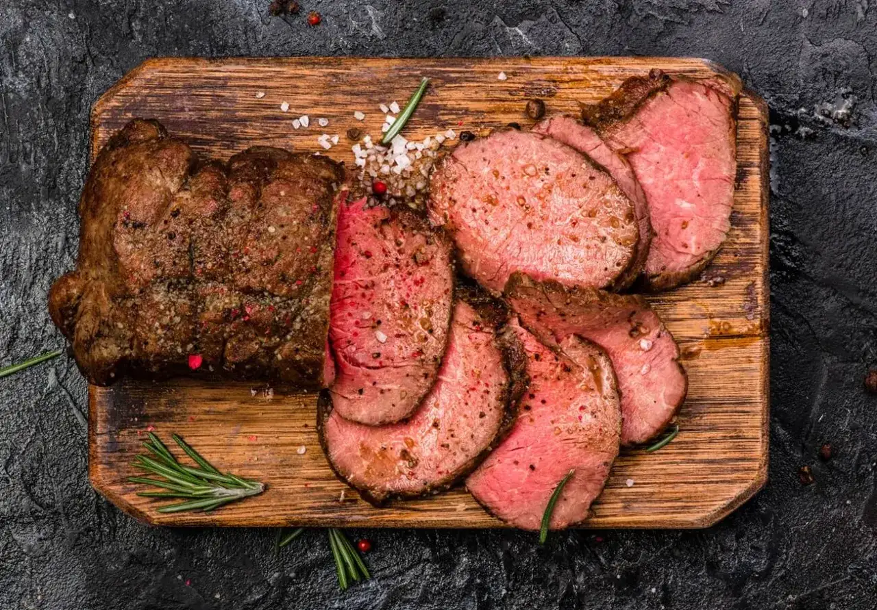 Perfekt gebratenes Roastbeef, in Scheiben geschnitten, mit grobem Salz und Rosmarin auf einem Holzbrett.