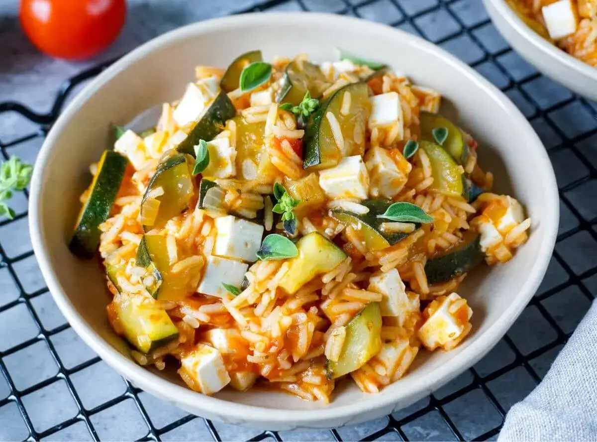 Herzhafte zucchini pfanne mit Reis, Feta und Kräutern, serviert in einer Schüssel.