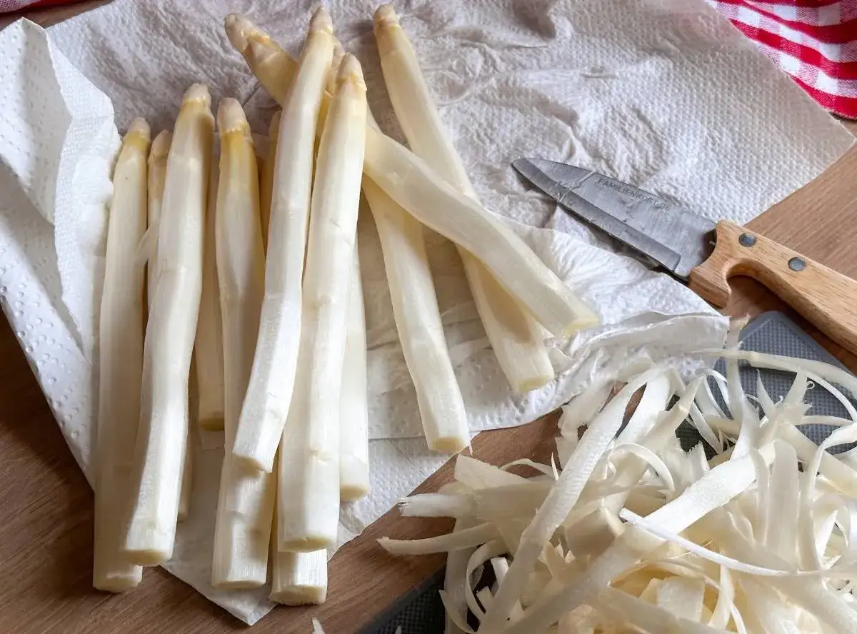 Frischer wei&szlig;er Spargel liegt auf K&uuml;chenpapier, bereit f&uuml;r die Zubereitung. Die Schalen liegen daneben. Perfekt f&uuml;r Spargelsuppe einfrieren.