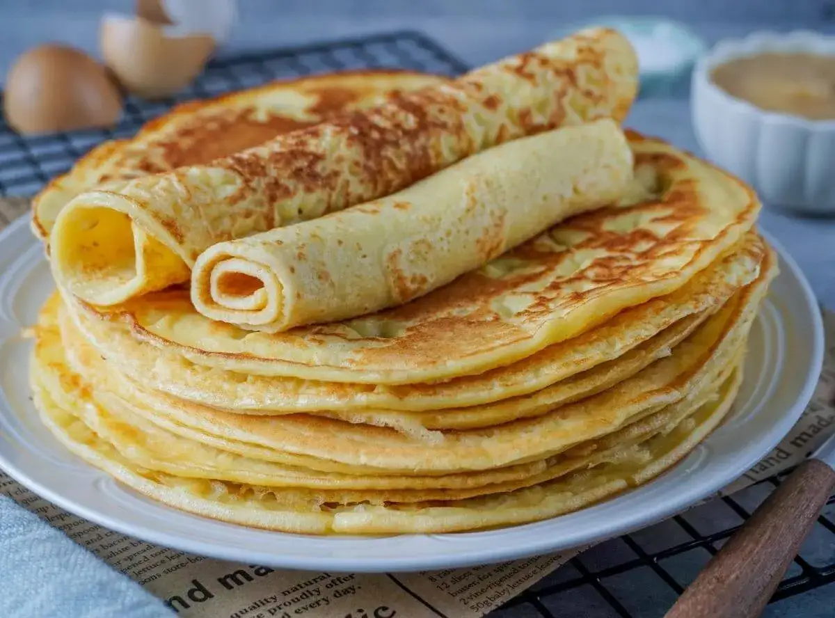 Ein Stapel goldbrauner Pfannkuchen, zwei davon gerollt, wie ein köstlicher Kuchen mit viel Eiern, der zum Genießen einlädt.