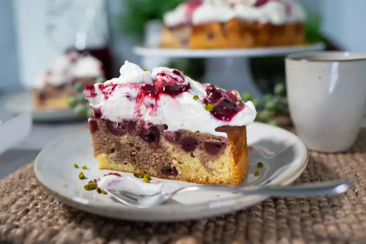 Ein Stück Marmorkuchen mit Kirschen und viel Sahne, garniert mit Kirschsoße und Pistazien. Ein Genuss!