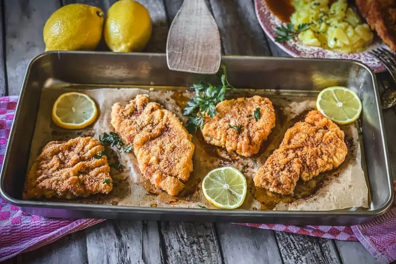 Vier goldbraune Schnitzel im Backofen, garniert mit Petersilie und Zitronenscheiben, warten auf ihre Beilage.