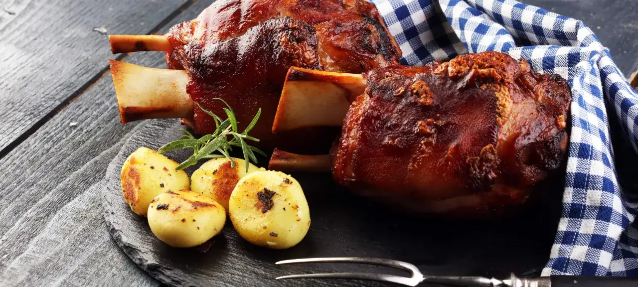 Zwei knusprige Kalbshaxen, ein Rosmarinzweig und goldbraune Kartoffeln – ein köstliches Kalbshaxe Rezept für Genießer.