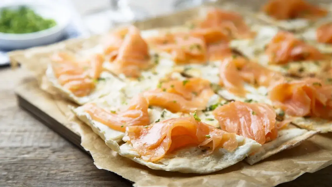 D&uuml;nner Flammkuchen mit zartem Lachs belegt, bestreut mit Kr&auml;utern. Ein Genuss f&uuml;r Augen und Gaumen.
