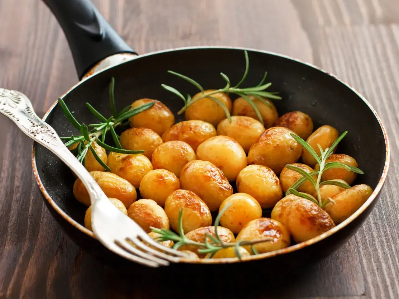 Kleine, goldbraune Kartoffeln mit Rosmarin in einer Pfanne. Die Drillinge sind perfekt gegart und bereit zum Servieren.