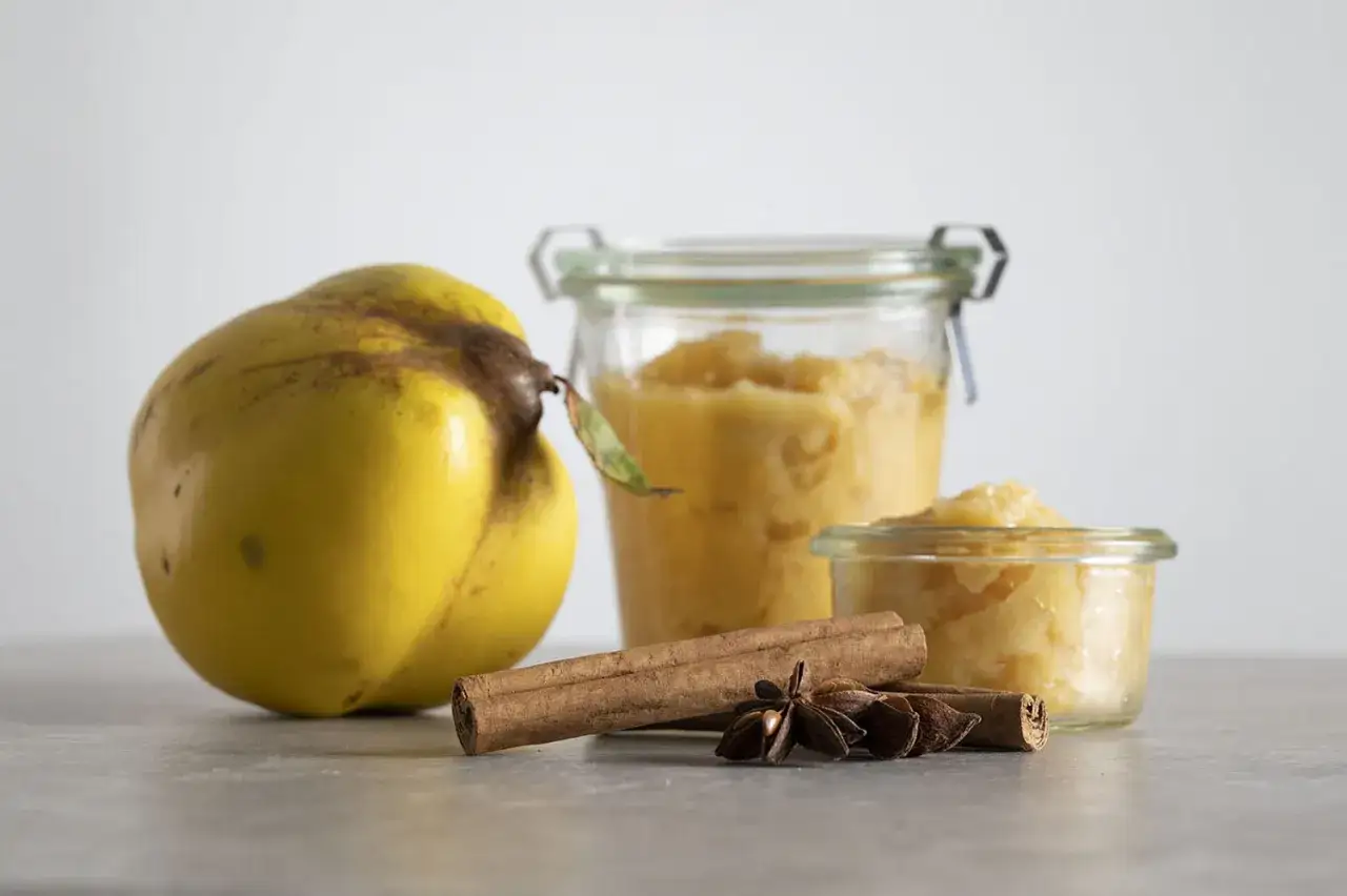 Ein gelber Quittenapfel neben zwei Gläsern mit Quittenkompott, Zimtstangen und Sternanis.