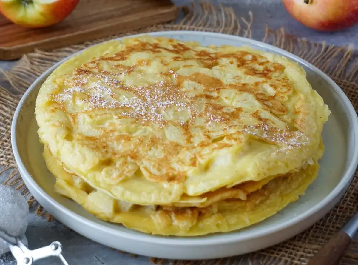 Omas Pfannkuchen-Rezept: goldbraune, fluffige Pfannkuchen mit Puderzucker bestäubt, serviert auf einem Teller.