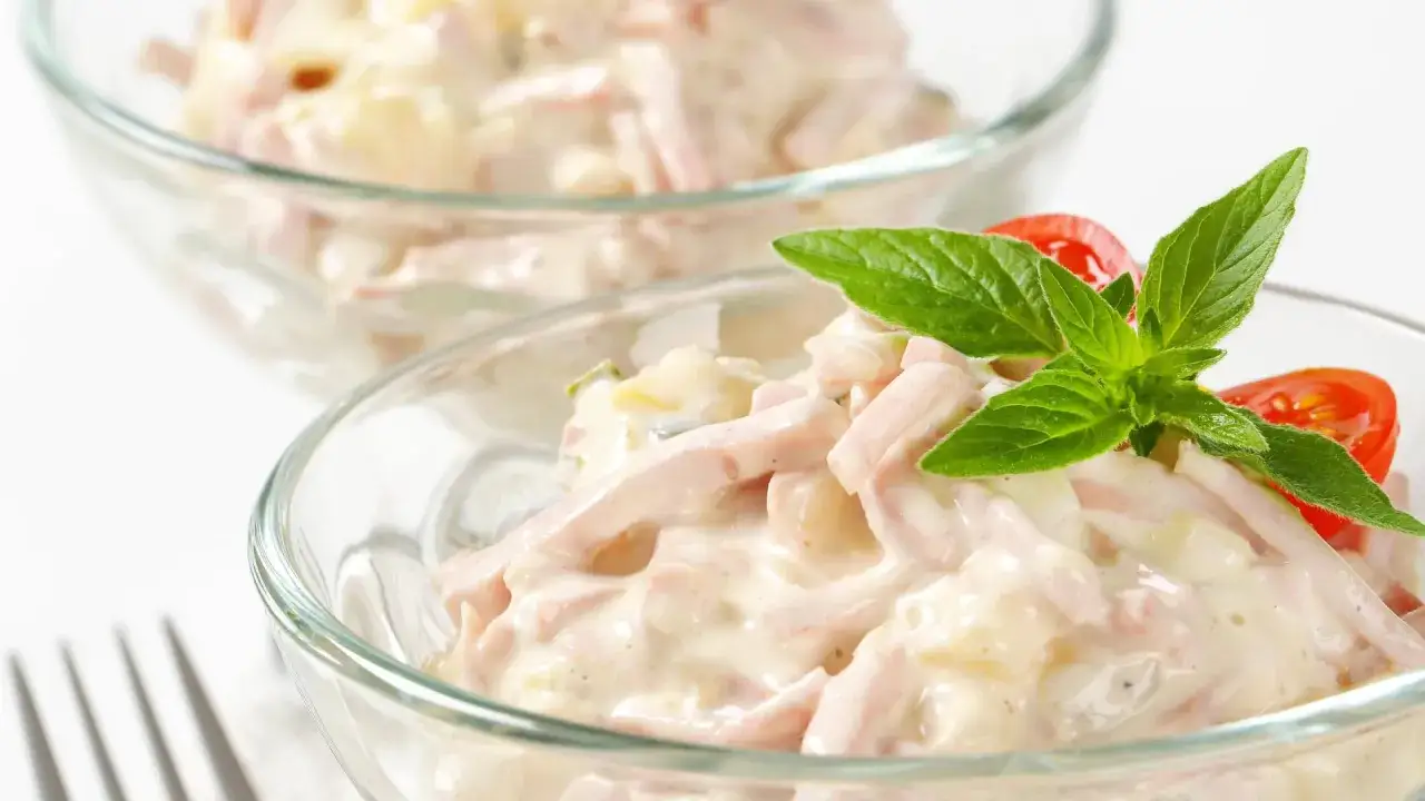 Zwei Schalen mit cremigem Kartoffelsalat mit Fleischsalat, garniert mit Minze und Tomaten.