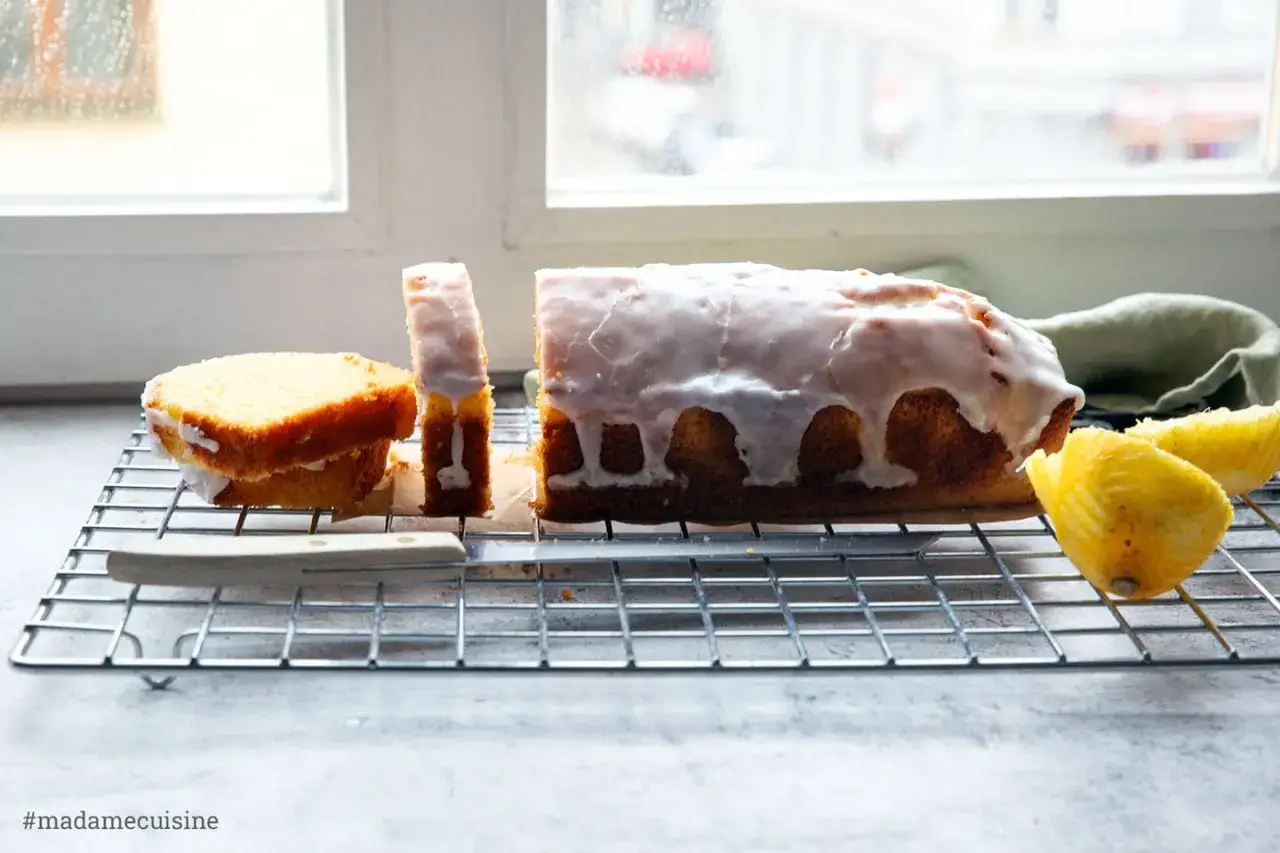 Ein saftiger Zitronenkuchen in Kastenform, mit Zuckerguss überzogen und angeschnitten. Daneben liegen frische Zitronenspalten.