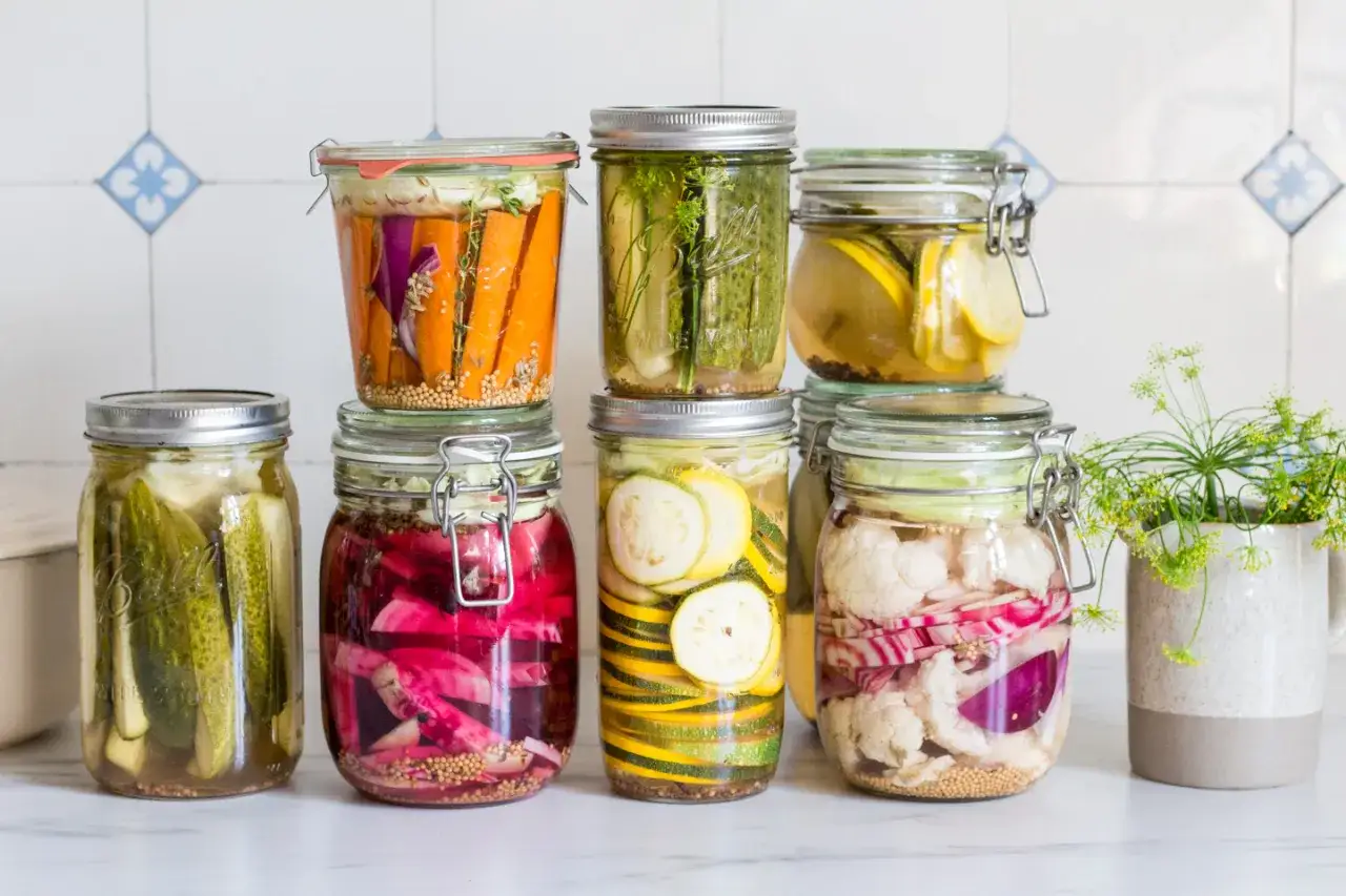Bunte Gläser mit saure bohnen einlegen im glas: Gurken, Karotten, Zucchini, Blumenkohl und rote Zwiebeln.