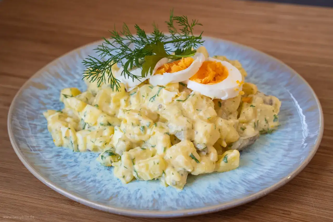 Ein cremiger Kartoffelsalat mit Mayo, garniert mit Dill und Ei, wartet auf dem Teller.