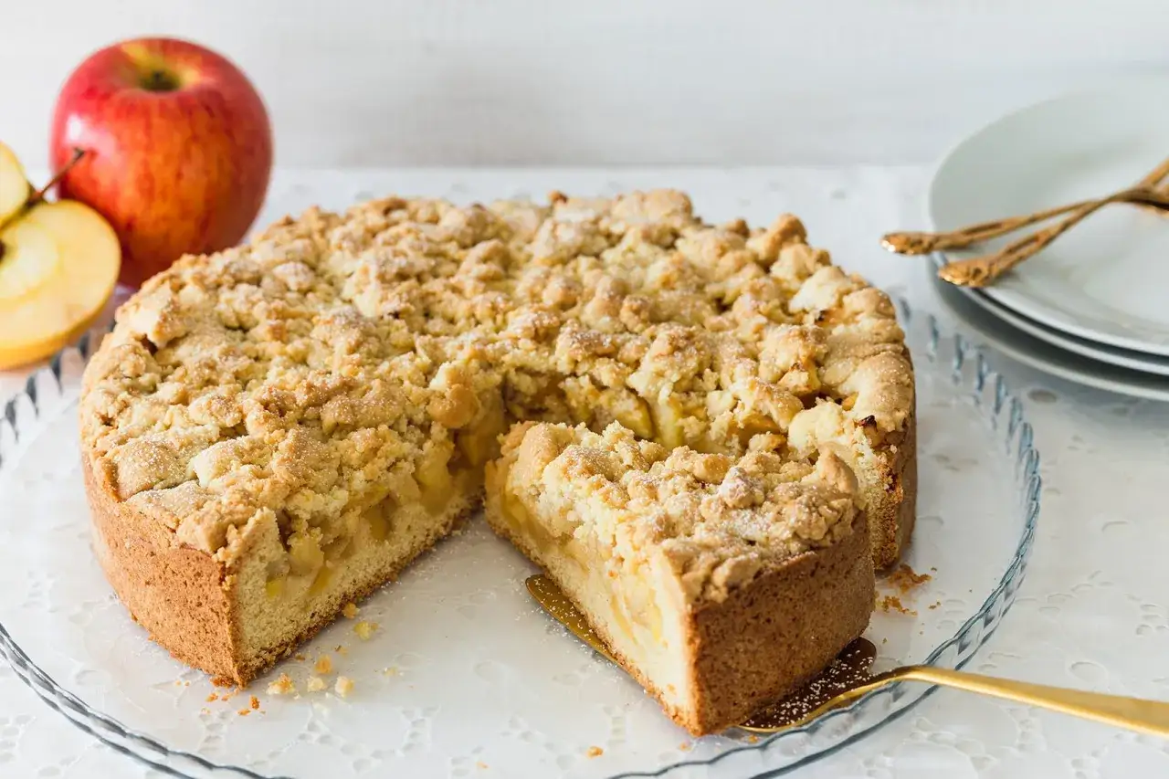 Ein saftiger Apfelkuchen mit Streuseln, frisch gebacken und bereit zum Genießen. Daneben liegen rote Äpfel.