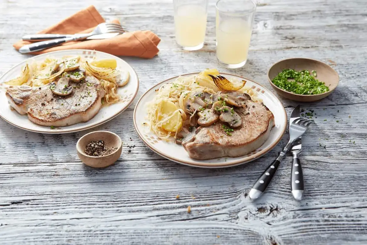 Zwei Teller mit saftigem Schweinefleisch, Sauerkraut, Pilzen und Kartoffeln, serviert als herzhaftes Szegediner Gulasch.