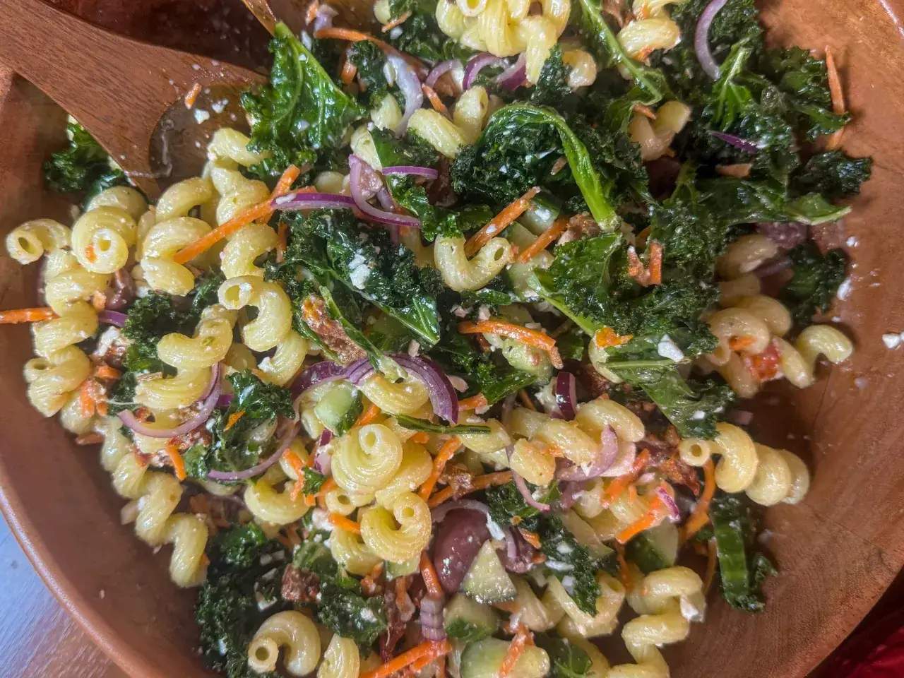 Leckerer nudelsalat ohne mayo mit Pasta, Grünkohl, Karotten und roten Zwiebeln in einer Holzschüssel.