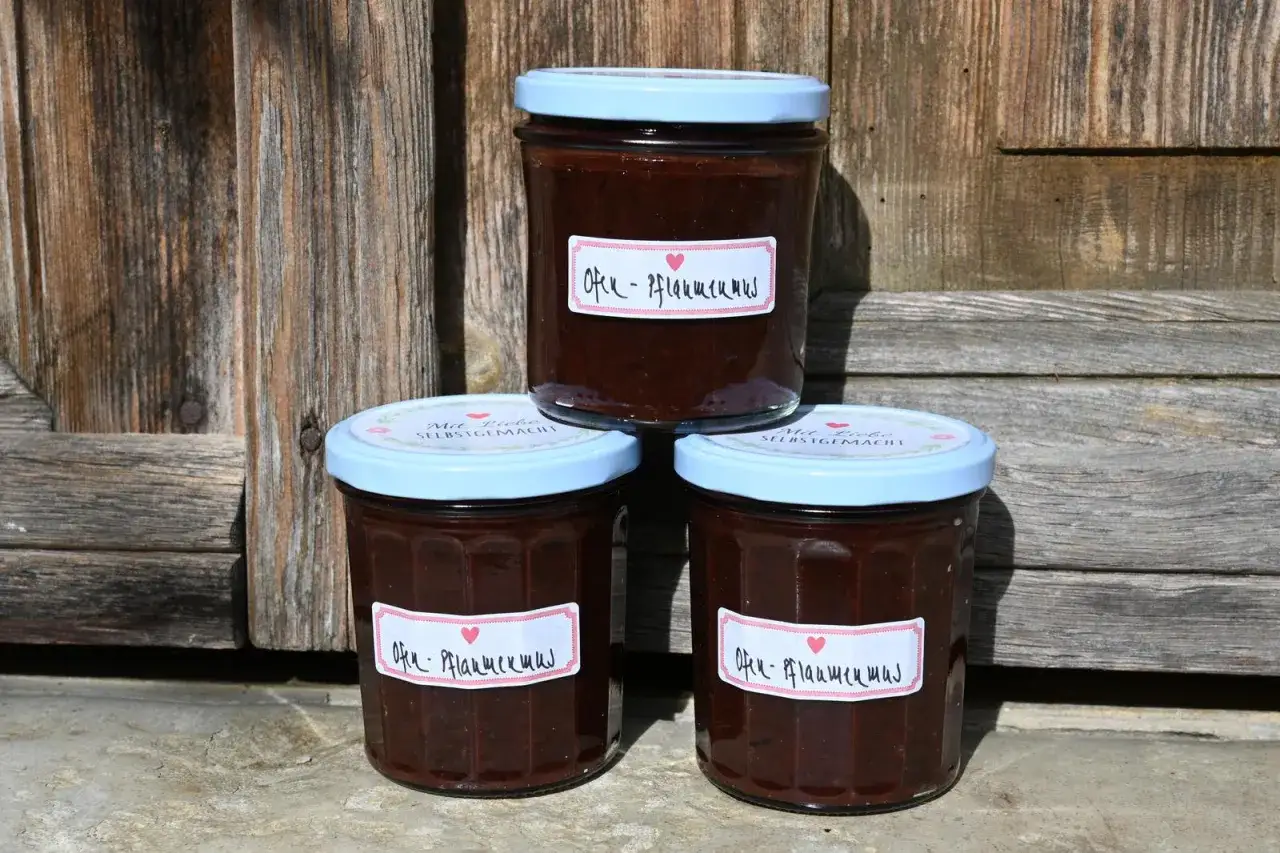 Drei Gläser mit selbstgemachtem Ofen-Pflaumenmus stehen vor einer Holzwand. Ein einfaches Rezept für süßen Genuss.