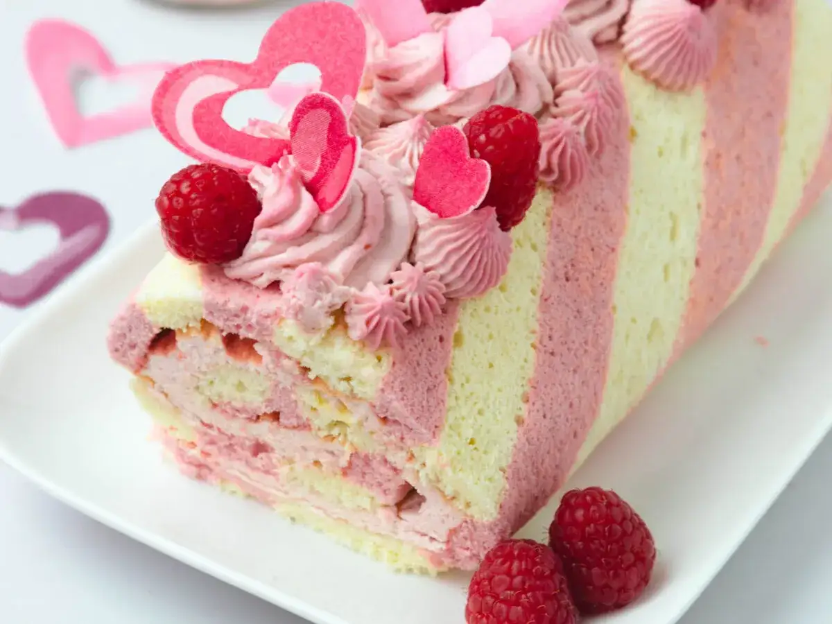 Himbeer Biskuitrolle mit rosa Creme, frischen Himbeeren und Herz-Dekorationen. Ein süßer Genuss für Verliebte.