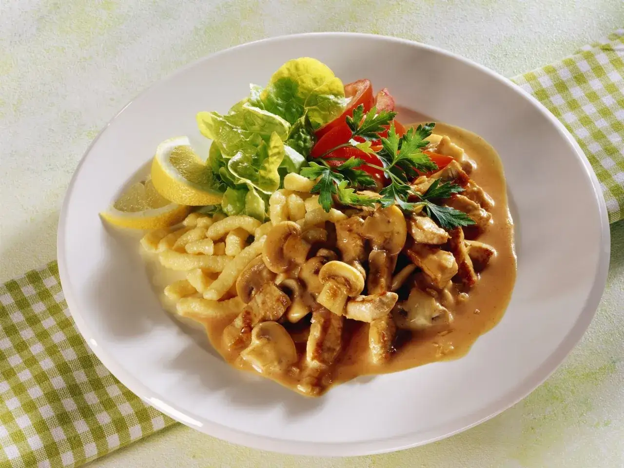 Putengeschnetzeltes mit Pilzen, serviert mit Spätzle, Salat und Zitronenspalten.