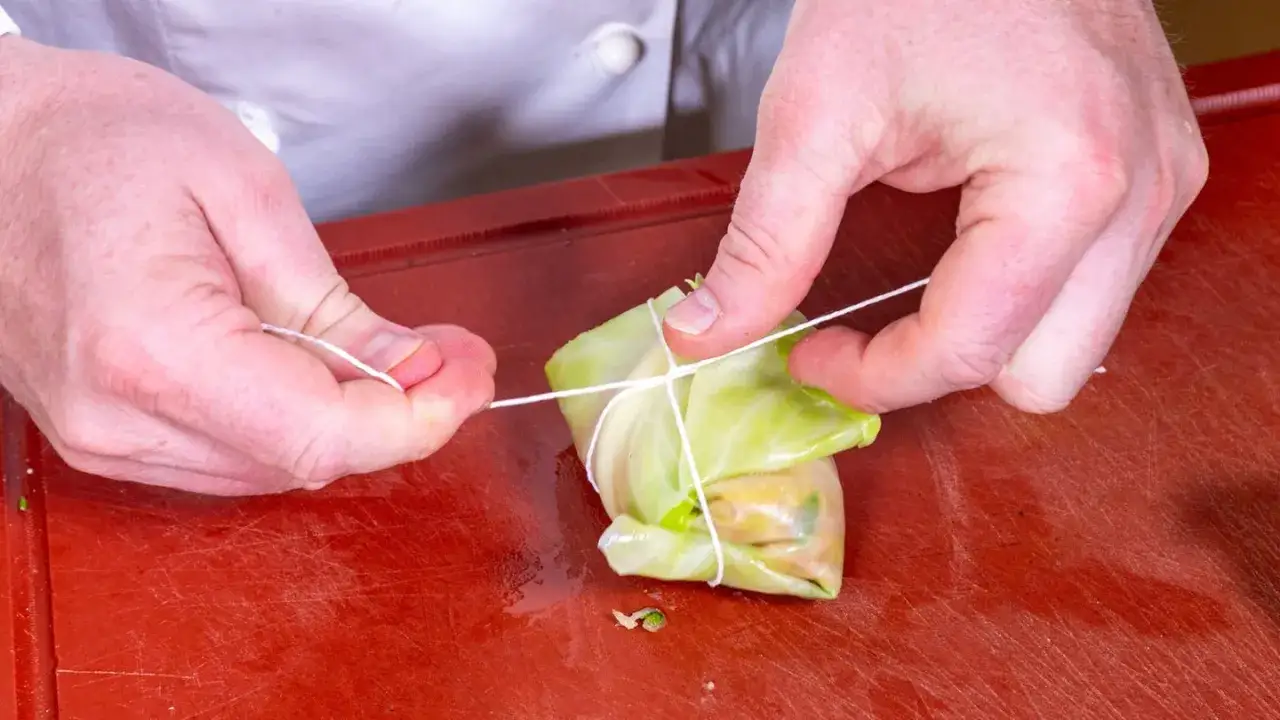 Hände binden Kohlrouladen mit Schnur. Ein wichtiger Schritt für das perfekte Kohlrouladen Rezept.