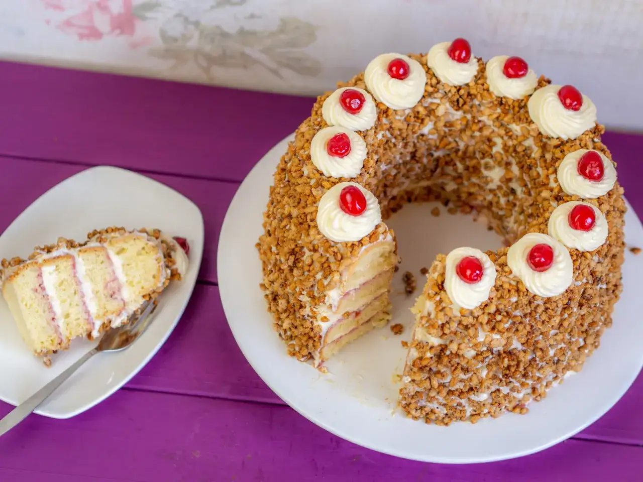 Ein Frankfurter Kranz Rezept vom Konditor: Biskuit mit Buttercreme, umhüllt von gehackten Nüssen und verziert mit Kirschen.