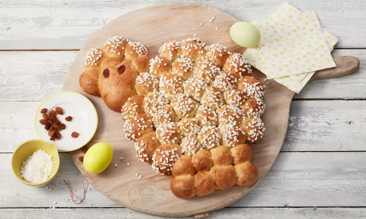 Ein süßes Osterlamm aus Hefeteig, bestreut mit Hagelzucker. Perfekt zum Backen zu Ostern, mit Rosinen als Augen und einem gelben Ei daneben.