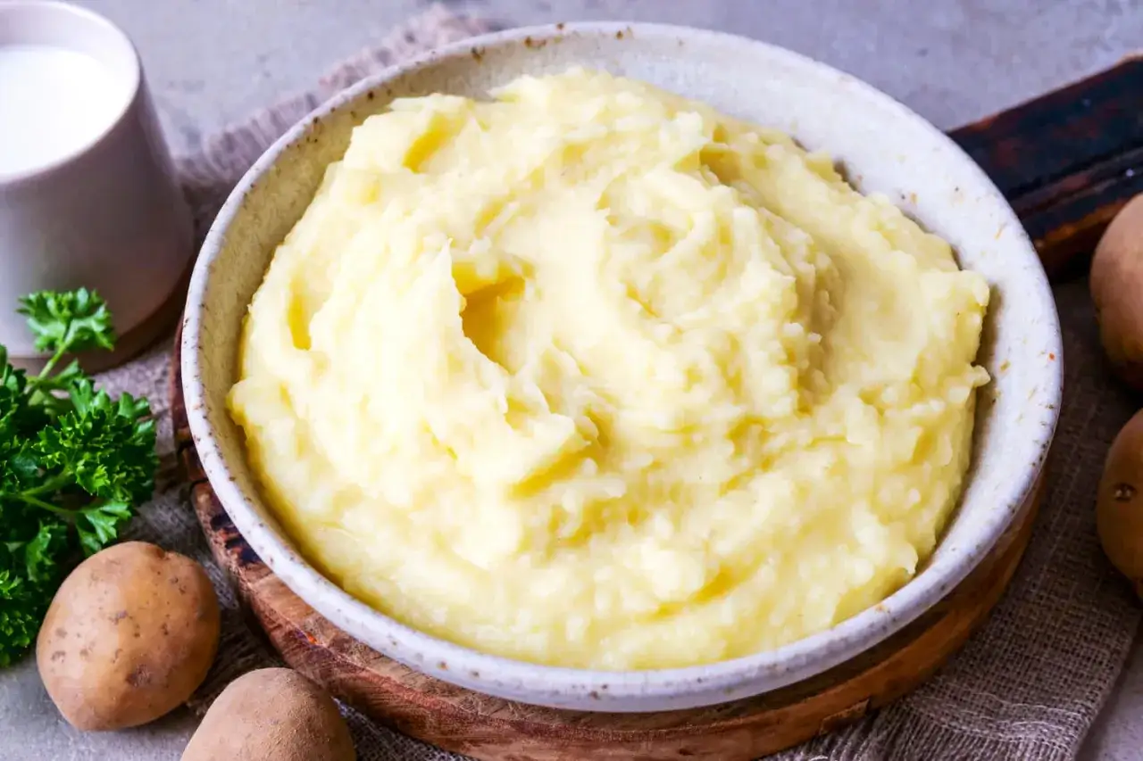 Cremiger kartoffelbrei ohne butter, serviert in einer Schüssel, mit frischer Petersilie und Kartoffeln daneben.