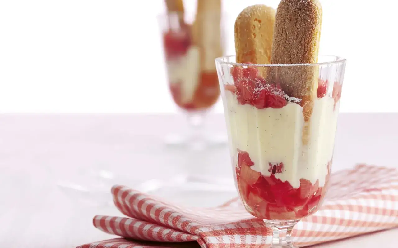 Ein Glas mit Rhabarber und Vanillepudding, garniert mit Löffelbiskuits. Ein köstlicher Rhabarber Pudding für den Sommer.
