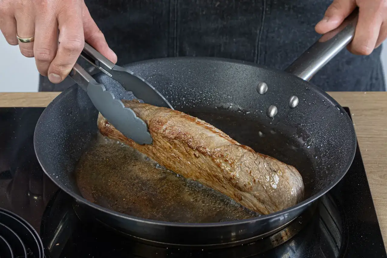 Ein saftiges Schweinefilet brät in der Pfanne. Einfache Rezepte für zartes Fleisch in der Pfanne gelingen so.