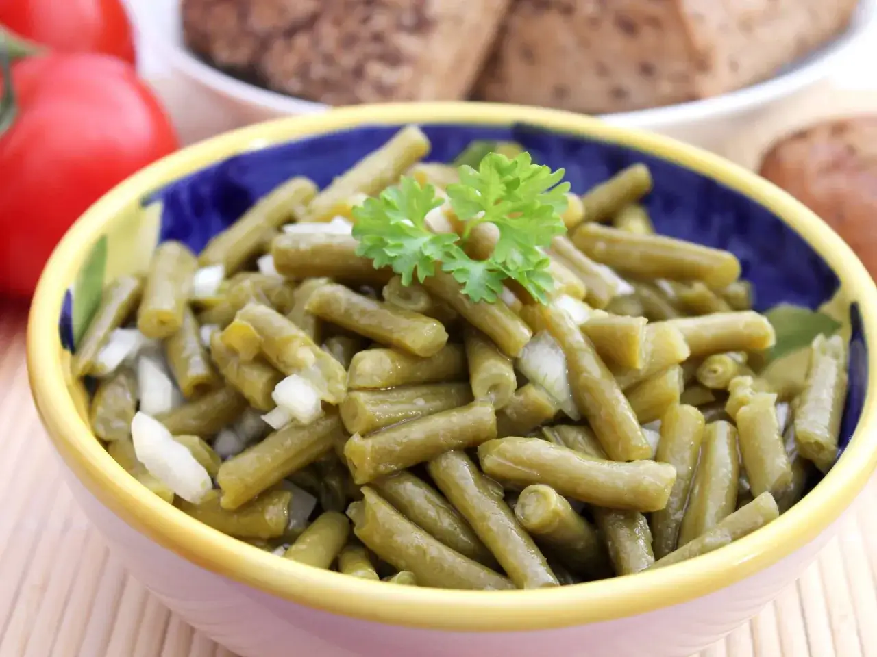 Omas Bohnensalat Rezept: Grüne Bohnen mit Zwiebeln und Petersilie in einer bunten Schüssel, daneben Tomaten und Brot.
