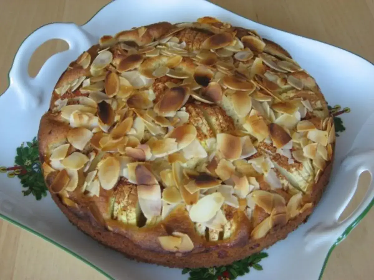 Ein köstlicher, kleiner Apfelkuchen mit gerösteten Mandelblättchen auf einer verzierten Servierplatte.