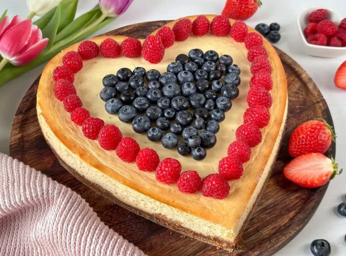 Herzförmiger Kuchen zum Muttertag, dekoriert mit Himbeeren und Blaubeeren. Ein süßes Dankeschön für die beste Mama!