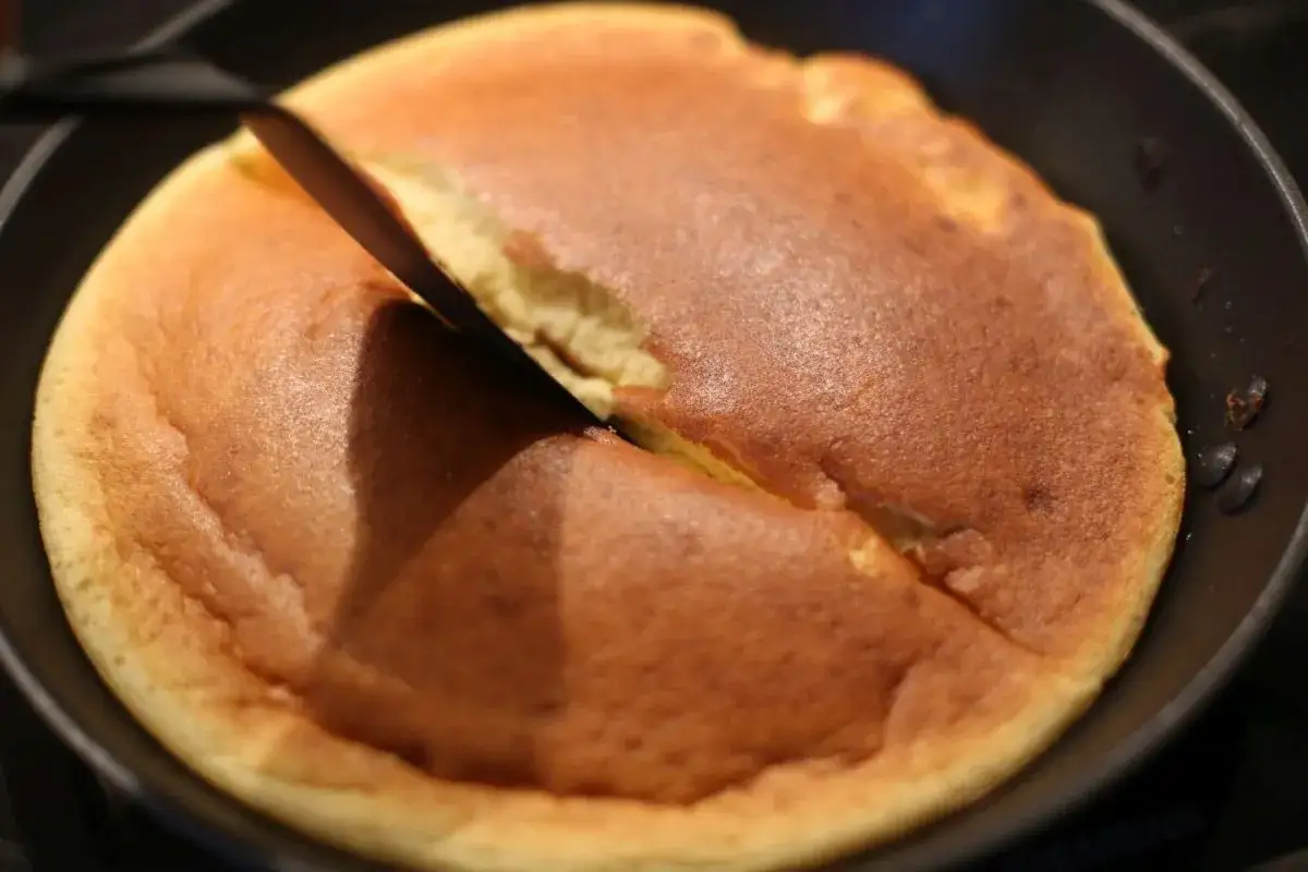 Ein goldbrauner, fluffiger Kaiserschmarrn wird in einer Pfanne mit einem Messer geteilt. Schneller Kaiserschmarrn im Backofen ist eine tolle Idee!
