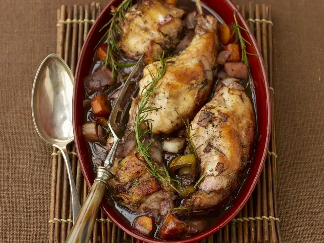 Klassisches Kaninchen-Rezept: Zartes Kaninchen in Rotwein geschmort mit Wurzelgemüse und Rosmarin, serviert in einer ovalen Auflaufform.
