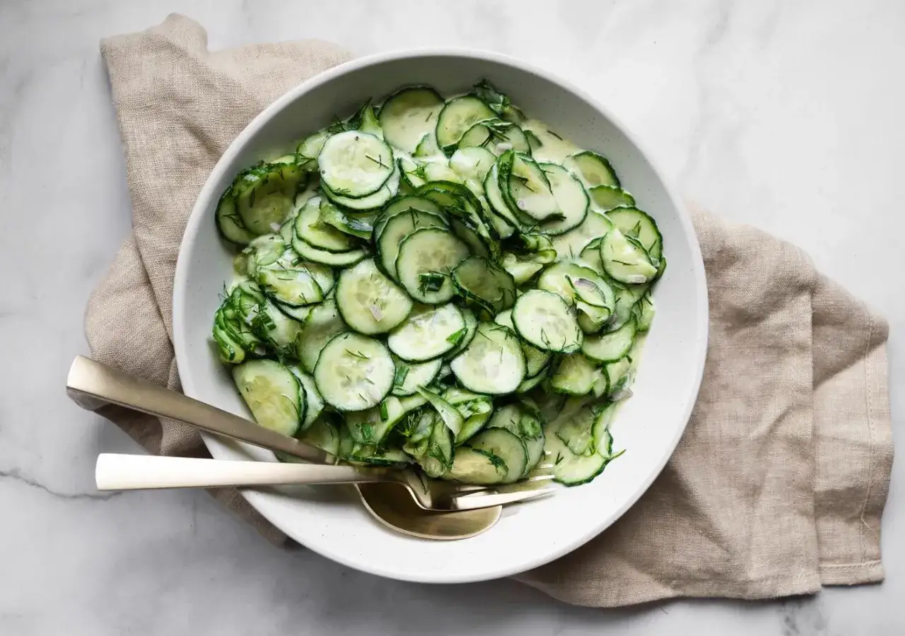 Frischer, cremiger Gurkensalat mit Dill und Zwiebeln, der beste Gurkensalat f&uuml;r hei&szlig;e Tage. Serviert mit goldenem Besteck.
