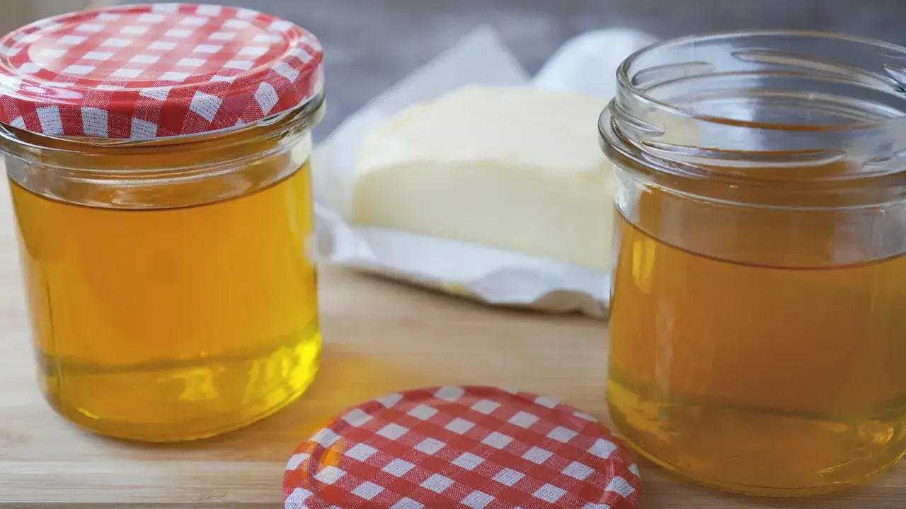 Zwei Gläser mit goldgelbem, klarem Fett und ein Stück Butter. Perfekt für butterschmalz selber machen.