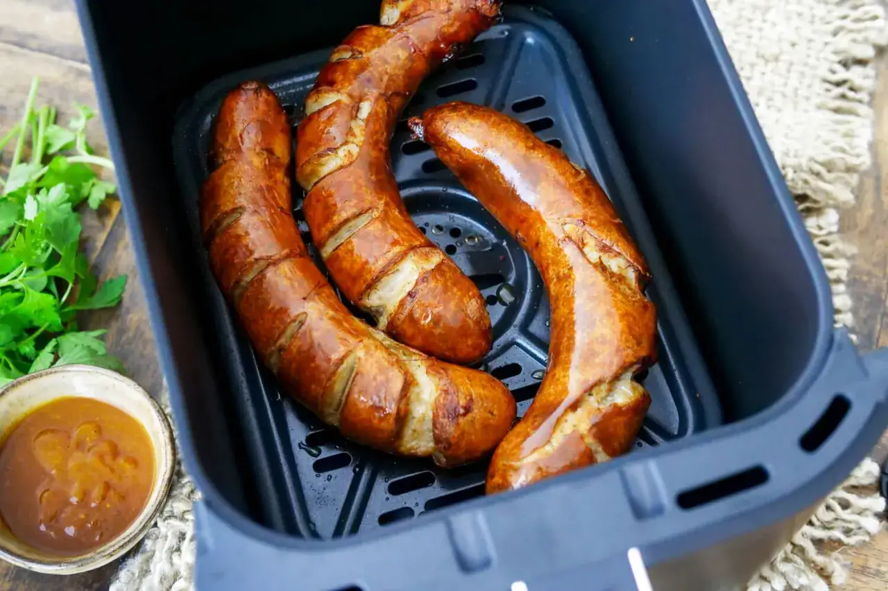 Drei goldbraune Bratw&uuml;rste im Airfryer, bereit zum Genie&szlig;en. Daneben eine Schale mit Sauce und frische Petersilie.