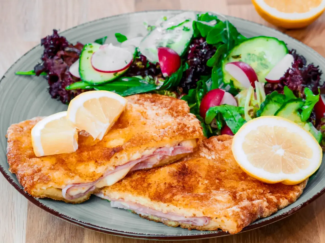Knuspriges Kartoffel Cordon Bleu mit Schinken und Käse, serviert mit frischem Salat und Zitronenspalten.