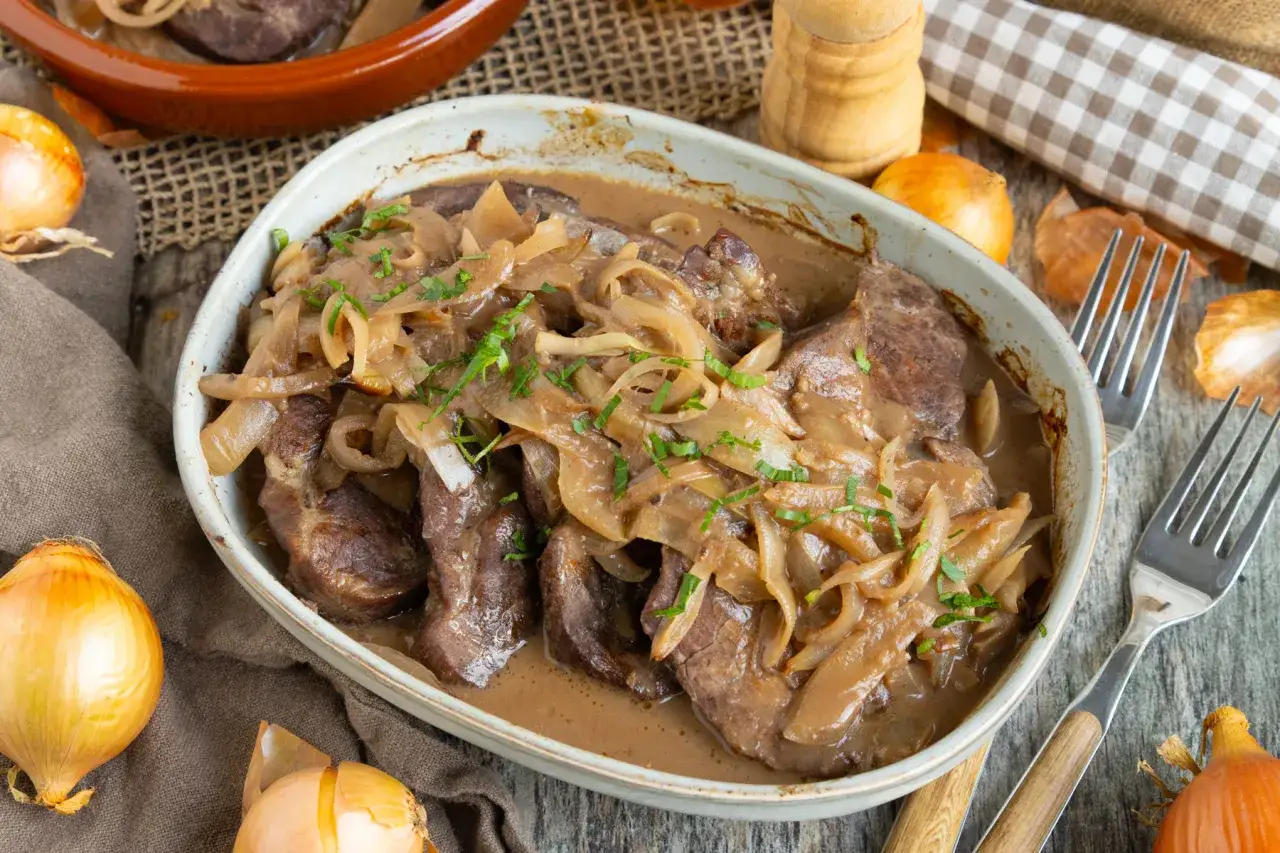 Herzhaftes Zwiebelfleisch-Rezept in einer Schmorpfanne, garniert mit Petersilie. Dazu passen frische Zwiebeln und Gabeln.