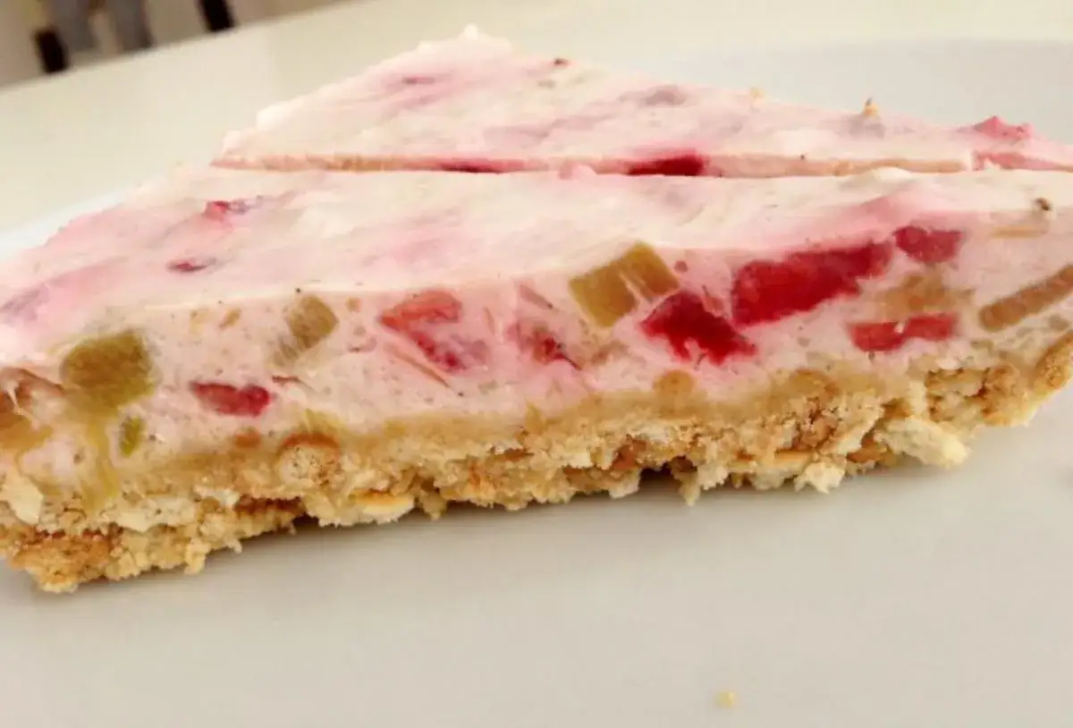 Zwei Stücke einer cremigen Erdbeer Rhabarber Torte auf einem weißen Teller. Der Boden ist knusprig, die Füllung rosa mit Fruchtstücken.
