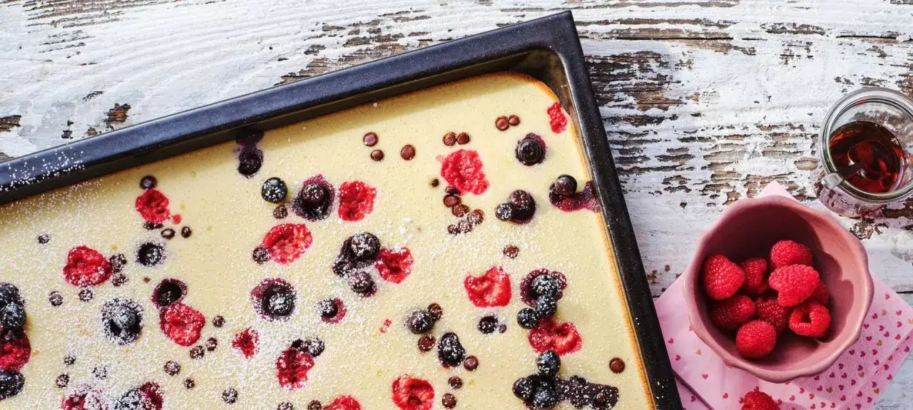 Frisch gebackener Ofenpfannkuchen mit Beeren und Puderzucker, bereit zum Servieren.