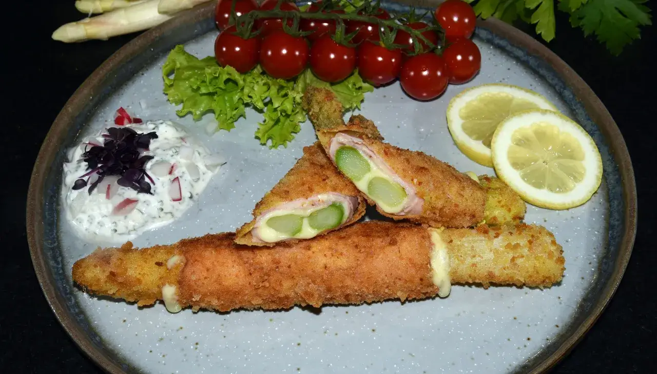 Knuspriges Spargel Cordon Bleu mit Schinken und Käse, serviert mit Dip, Kirschtomaten und Zitrone.