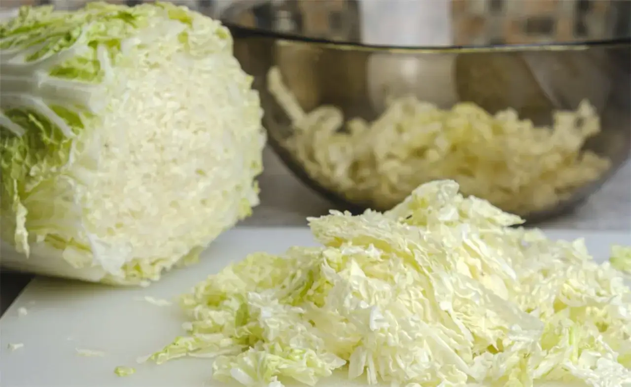 Ein halber Chinakohl liegt auf einem Schneidebrett, daneben ein Haufen geschnittener Chinakohl. Perfekt für leckere Chinakohl Rezepte!